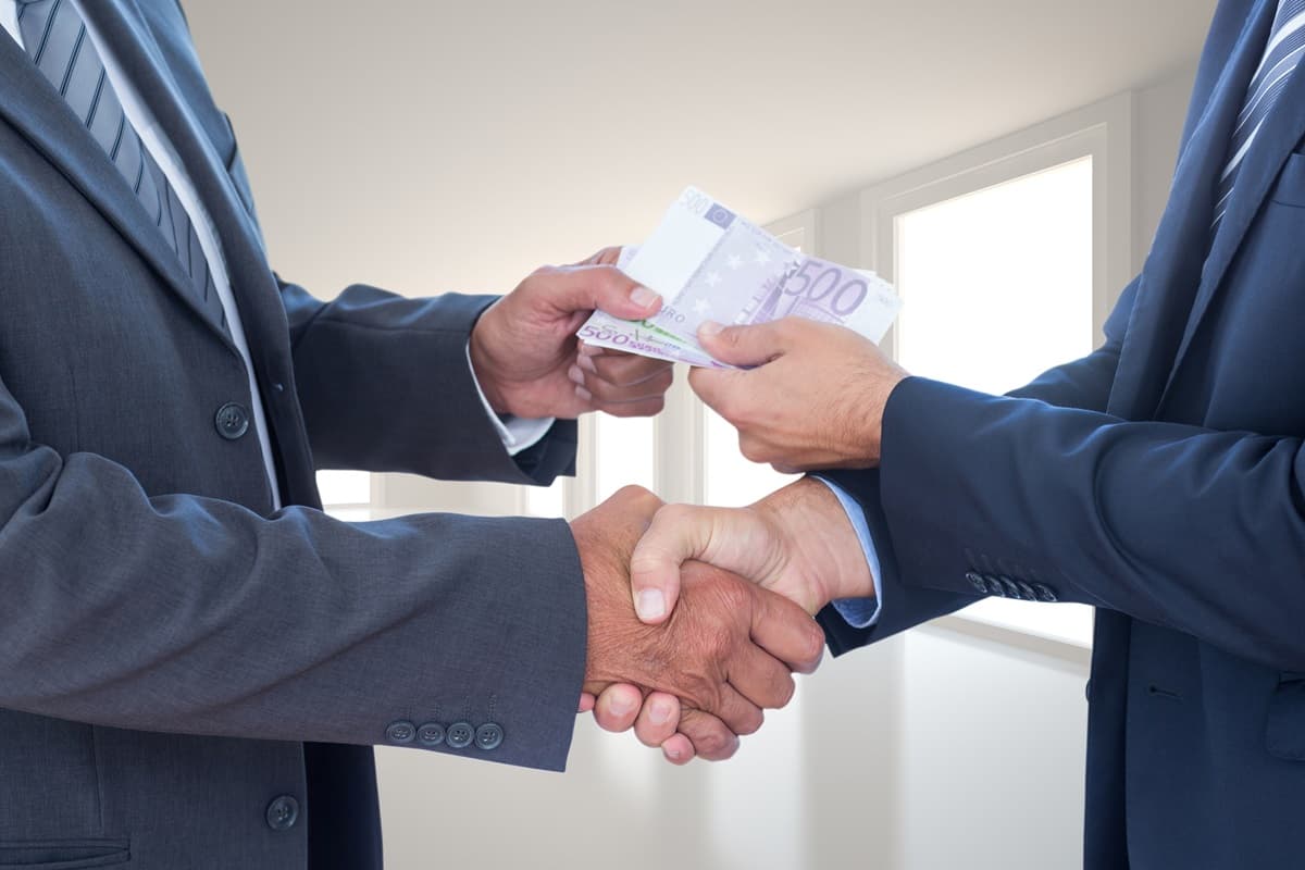 Due uomini si passano una mazzetta di banconote mentre si stringono la mano: simbolo di un accordo contrario ai principi anticorruzione definiti dalla certificazione 37001.