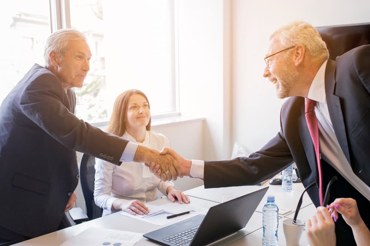 Due uomini si stringono la mano in un ufficio, in presenza di due collaboratrici.