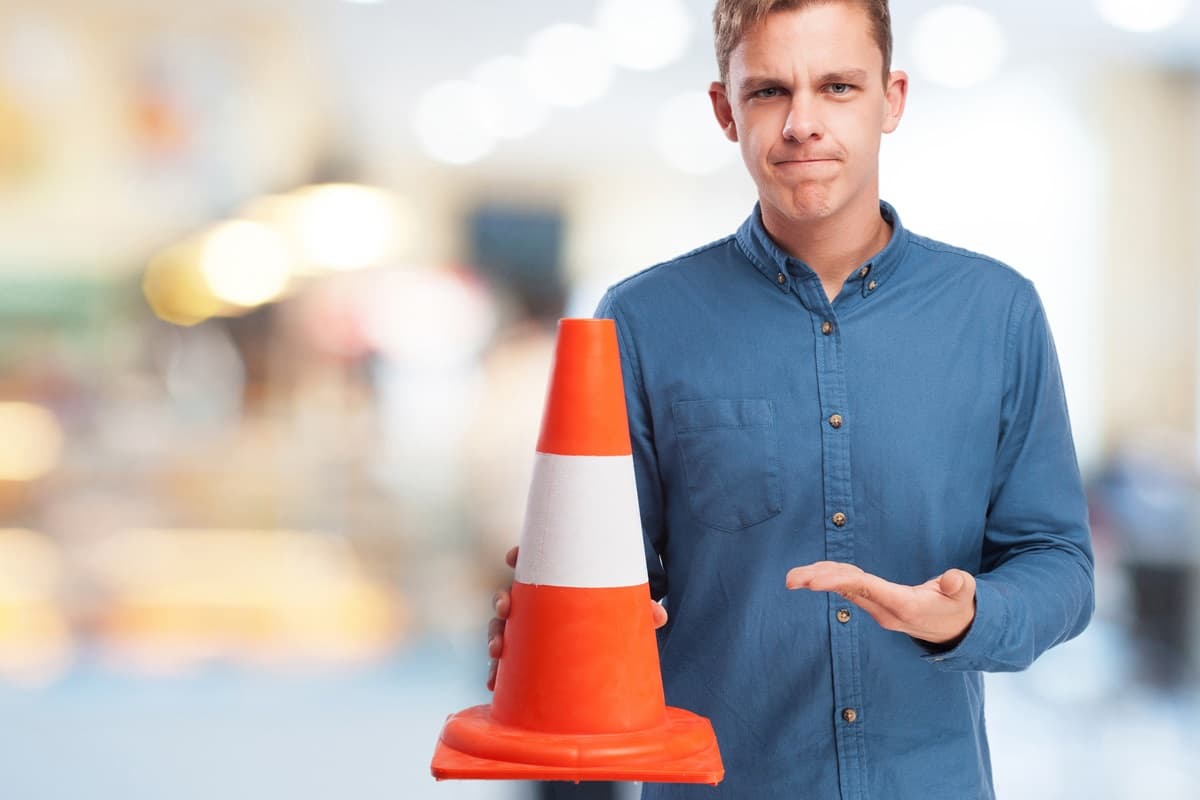 Un ragazzo che tiene un cono stradale in una mano e lo indica con l'altra: la gestione della segnaletica temporanea è uno degli aspetti di cui occuparsi per la ISO 39001.